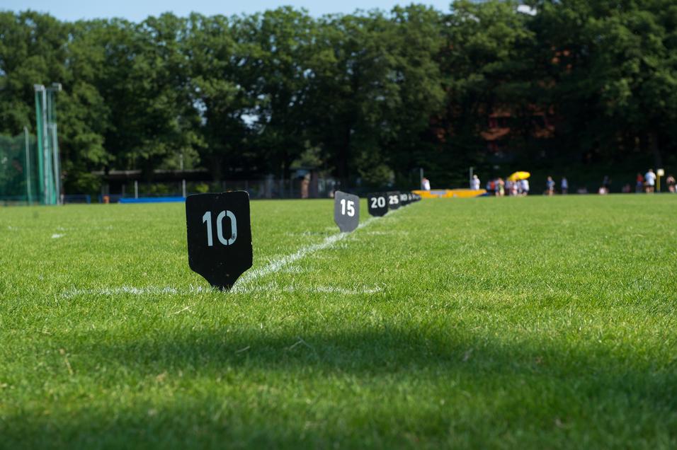 Einfache Rasenfläche mit markierten Metern, die auf einen Wettkampfbereich im Hintergrund hinweisen.
